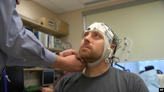 In this Nov. 20, 2019 image from video, Zach Ault is fitted with an EEG cap which uses electrodes to track the electrical activity of his brain, at the National Institutes of Health's hospital in Bethesda, Md. (AP Photo/Federica Narancio)