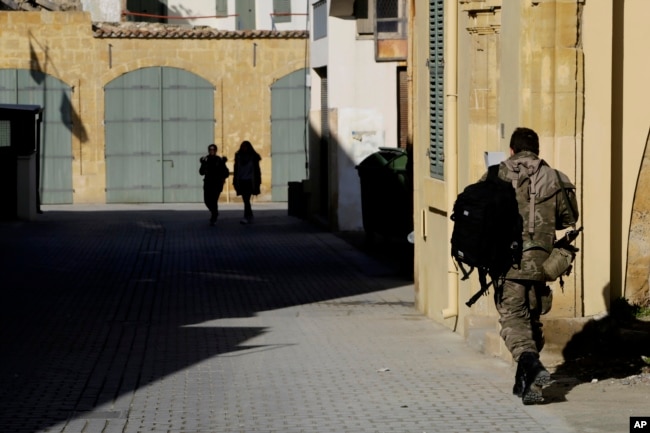 FILE - A Greek Cypriot soldier (R) walks towards a military guard post across the U.N. buffer zone that divides the Greek and Turkish Cypriots controlled areas, in the divided capital of Nicosia, Cyprus, Jan. 12, 2017.