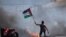 Un manifestante ondea la bandera palestina durante los enfrentamientos con las fuerzas israelíes en el puesto de control de Hawara, al sur de la ciudad cisjordana de Naplusa, el viernes 14 de mayo de 2021.