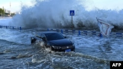 Automobil se probija kroz vodu dok se talasi, izazvani tajfunom In-Fa, razbijaju o obalu, u Kvingdaou, Kina, 25. jula 2021. (Photo by STR / AFP)