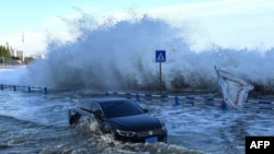 A car sits in floodwaters as waves, caused by Typhoon In-Fa further down the Chinese coast, surge over a barrier along the seacoast in Qingdao in China's eastern Shandong province July 25, 2021.