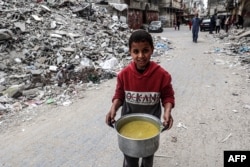A boy walks past the rubble of a collapsed building with a pot of food provided by a charity organization ahead of the fast-breaking "iftar" meal during the Muslim holy month of Ramadan in Rafah, Gaza Strip, on March 16, 2024.