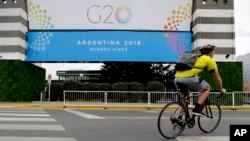 A man rides a bicycle past a banner promoting the G20 summit at the Costa Salguero Center, in Buenos Aires, Argentina, Nov. 27, 2018. 