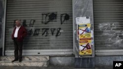 A man stands outside a shuttered shop next a poster that reads "Yes to Work, No to the Euro," Athens, Nov. 12, 2012.
