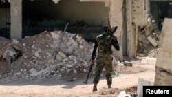 A Free Syrian Army fighter carries weapons as he walks past damaged buildings in a rebel-held part of the southern city of Deraa, Syria July 9, 2017.