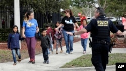 Una oficina de policía de Seguridad Nacional detiene el tráfico cuando personas cruzan la calle con niños en las afueras de una instalación del Servicio de Inmigración y Control de Aduanas de Estados Unidos, el miércoles 9 de enero de 2019