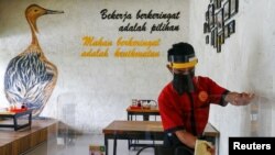 Seorang karyawan mengenakan masker dan pelindung wajah membersihkan pembatas di sebuah meja makan di restoran seiring dengan pembukaan masa PSBB transisi di Jakarta, Senin, 12 Oktober 2020. (Foto: Reuters)