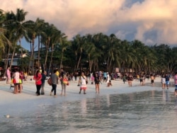 FILE - Tourists visit a beach during sunset in Boracay, Philippines, Oct. 26, 2018.