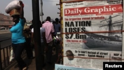 People walk past a vendor selling newspapers with its front page reporting about an Argentine naval vessel involved in a debt dispute, in Accra, Ghana, December 2012.