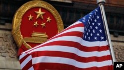 FILE - In this Nov. 9, 2017, file photo, an American flag is flown next to the Chinese national emblem during a welcome ceremony for visiting U.S. President Donald Trump outside the Great Hall of the People in Beijing. 