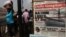 People walk past a vendor selling newspapers with its front page reporting about an Argentine naval vessel involved in a debt dispute, in Accra, Ghana, December 2012.
