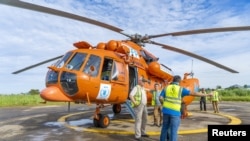 Humanitarian workers discuss near a United Nations Humanitarian Air Service (UNHAS) helicopter painted in orange color as part of efforts to improve safety of operations in the restive eastern Democratic Republic of Congo in this photograph released on April 20, 2023.
