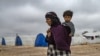 An elderly displaced Syrian woman carries a child in the Washukanni Camp for the internally displaced people near the predominantly Kurdish city of Hasakeh in northeastern Syria.