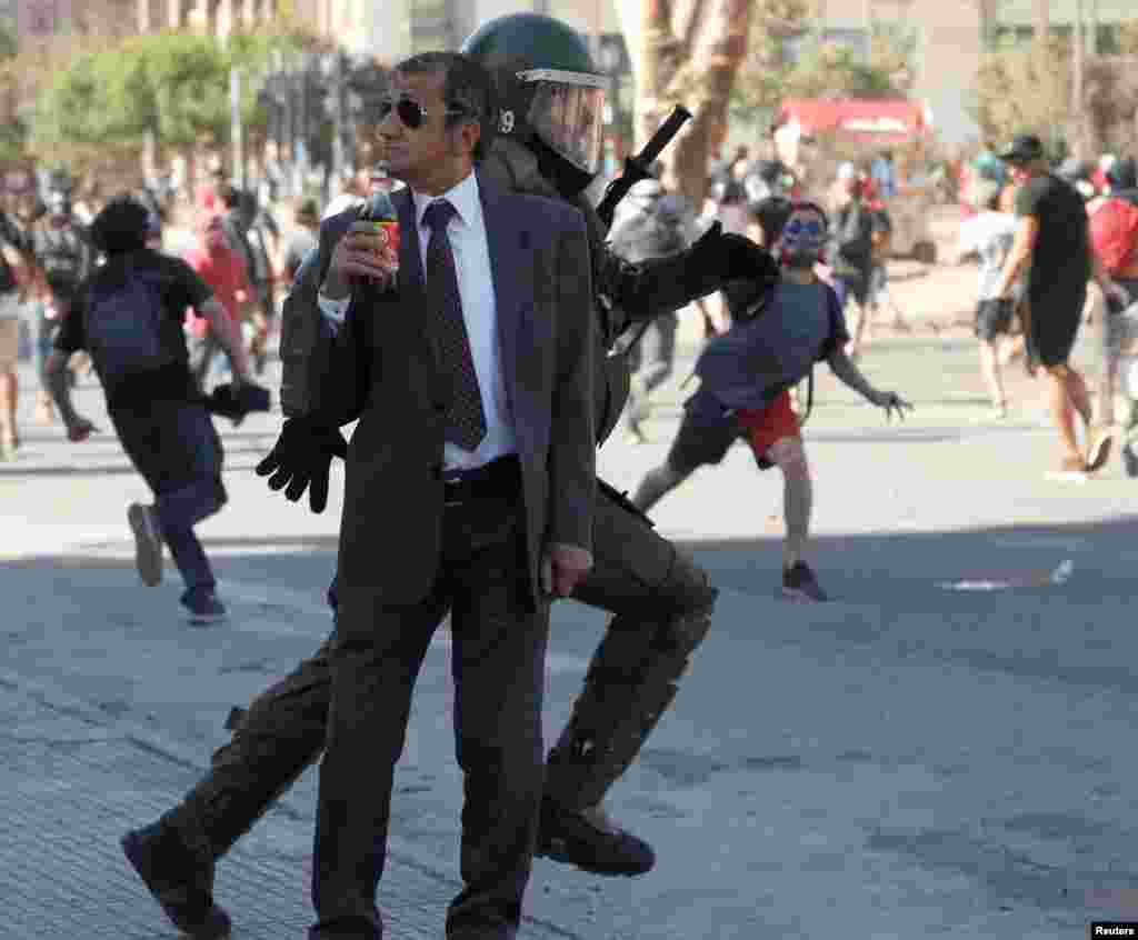 A man drinks a Frucola as a policeman chases demonstrators during a protest against Chile&#39;s government in Santiago, Dec. 4, 2019.