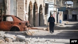 A woman walks with a cane past a destroyed car down a street in Al-Hirak in the eastern Daraa province countryside in southern Syria, June 21, 2018.