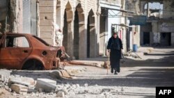 A woman walks with a cane past a destroyed car down a street in Al-Hirak in the eastern Daraa province countryside in southern Syria, June 21, 2018.