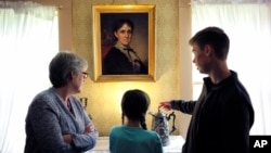 FILE - Museum visitors stand near a portrait of author Louisa May Alcott by American artist George Healy at Orchard House, in Concord, Mass., May 17, 2018. 