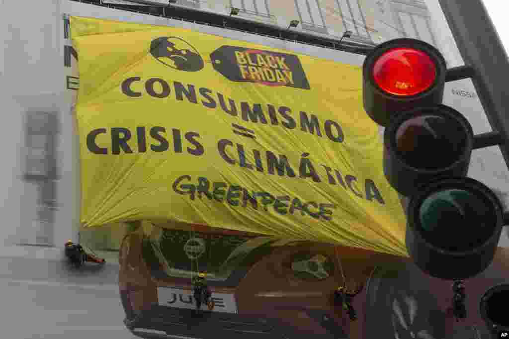 Activistas de Greenpeace cuelgan una pancarta gigante que cubre el anuncio de un automóvil que dice &#39;Consumo es igual a la crisis climática&#39; durante una venta del Black Friday en Madrid, España, el viernes 29 de noviembre de 2019.