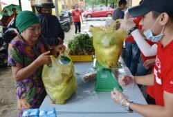 Kechara staff help a woman with a bag of produce at one of the charity's mobile food banks in Kuala Lumpur. (Zsombor Peter/VOA)