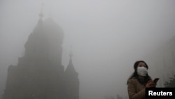 Seorang wanita mengenakan masker saat melewati gereja San Sophia di kota Harbin, China yang tertutup kabut tebal akibat asap polusi (21/10). 