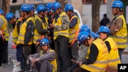 Workers wait for transport outside a construction site in Beijing, Tuesday, April 9, 2024.