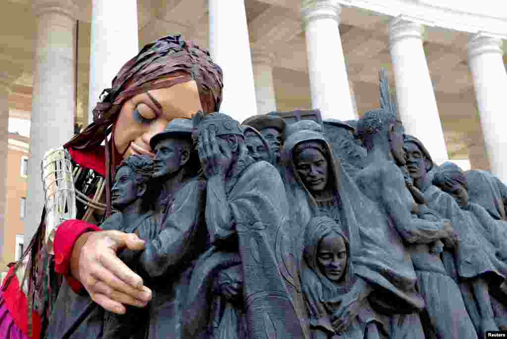 Little Amal, a 3.5-meter-tall puppet of a young Syrian refugee girl, embraces the Angels Unawares scuplure in St. Peter&#39;s Square at the Vatican, as she travels across Europe to raise awareness for the plight of young refugees.