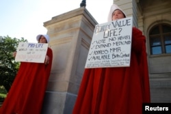 April Houston dan Lara Martin memegang poster sambil mengenakan kostum Handmaid atau pelayan perempuan dalam unjuk rasa memprotes RUU anti-aborsi negara bagian Georgia, di Georgia State Capitol di Atlanta, Georgia, 7 Mei 2019.