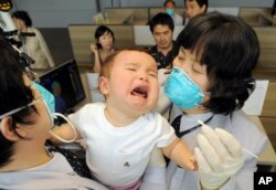 FILE - South Korean quarantine officers try to take samples of a baby arriving from the US at Incheon airport, west of Seoul.