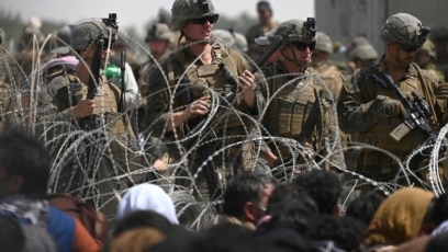 Para tentar AS berjaga di balik kawat berduri, sementara warga Afghan duduk di pinggir jalan dekat kawasan militer Bandara Internasional Kabul, 20 Agustus 2021.