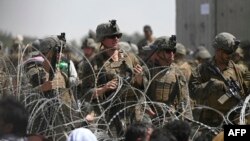 Tentara AS berjaga di balik kawat berduri saat warga Afghanistan duduk di pinggir jalan dekat bagian militer bandara di Kabul pada 20 Agustus 2021. (Foto: AFP/Wakil Kohsar)