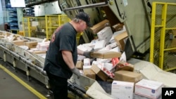 FILE - A postal worker arranges packages on a conveyor belt at the main post office in Omaha, Neb., Dec. 14, 2017.