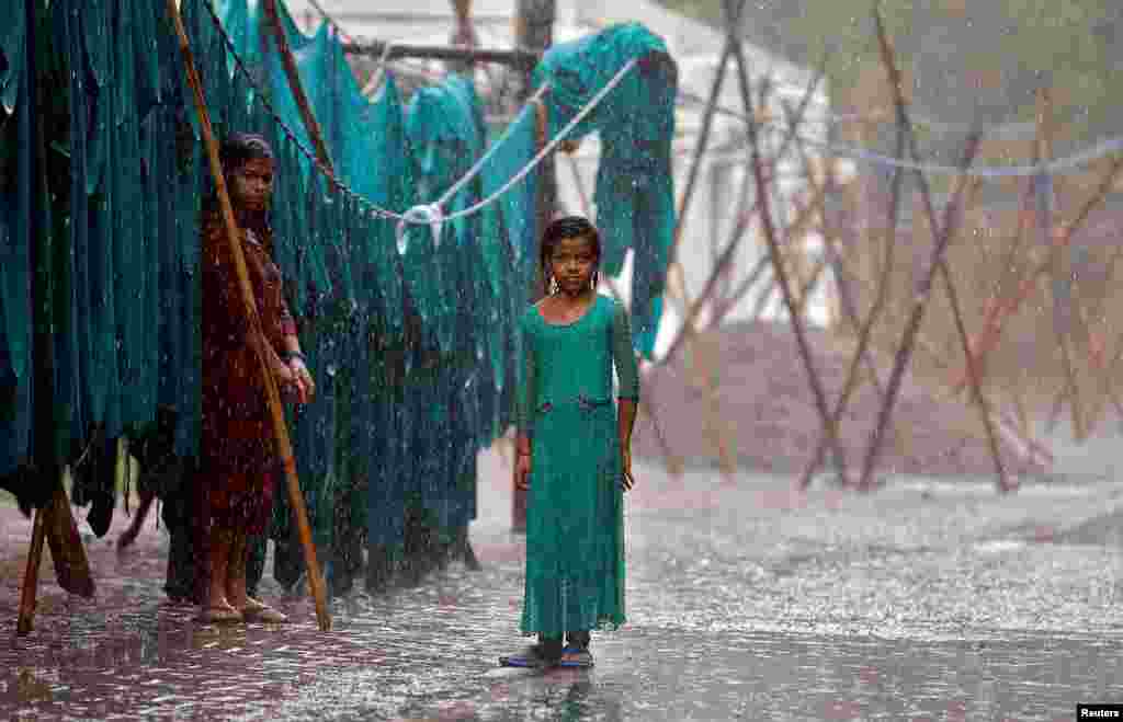 Seorang anak perempuan berdiri saat hujan akibat angin muson di sebelah layanan laundry di New Delhi, India.