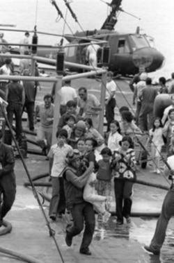 U.S. Marine helicopter crewmen carry Vietnamese civilians to safety aboard the U.S.S. Blue Ridge on April 29, 1975. Their evacuation helicopter crashed on the deck of the amphibious command ship.