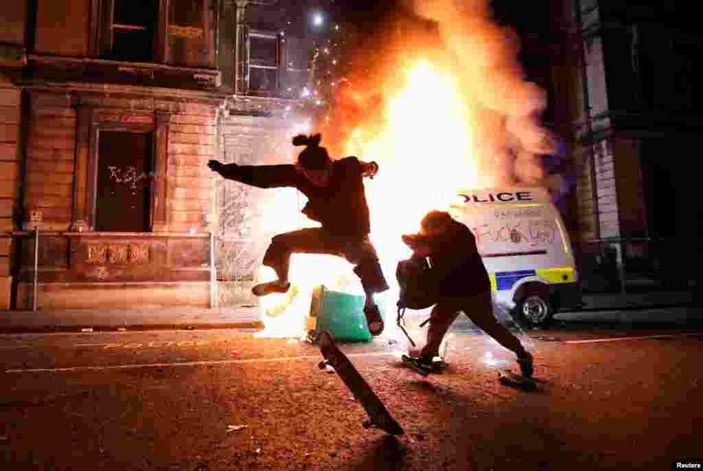 A demonstrator skateboards in front of a burning police vehicle during a protest against a new proposed policing bill, in Bristol, Britain, March 21, 2021.