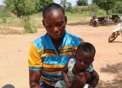 Adama Tapsoba sits with her child on her lap outside a small clinic in Gampela village on the outskirts of Burkina Faso's capital, Ouagadougou, Saturday Oct. 10, 2020.