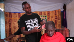 Jerome Mbusuka uses clippers powered by electricity from solar panels to cut hair. (M. Yusuf/VOA)