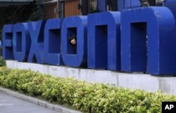 FILE - A worker looks out through the logo at the entrance of the Foxconn complex in the southern Chinese city of Shenzhen, May 27, 2010.