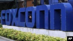 FILE - A worker looks out through the logo at the entrance of the Foxconn complex in the southern Chinese city of Shenzhen, May 27, 2010. 