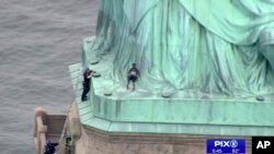 In this image made from video by WPIX-TV, a woman leans against the robes of the Statue of Liberty on Liberty Island, as a police officer stands on a ledge nearby, talking the climber into descending, in New York, July 4, 2018.