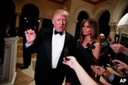 President-elect Donald Trump talks to reporters during a New Year's Eve party at Mar-a-Lago, Dec. 31, 2016, in Palm Beach, Fla. His wife, Melania Trump, looks on.