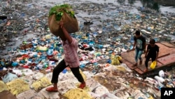 FILE - A man carries a sack of vegetables as he walks past a polluted canal littered with plastic bags and other garbage in Mumbai, India.