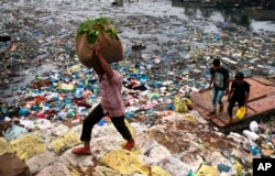 FILE - A man carries a sack of vegetables as he walks past a polluted canal littered with plastic bags and other garbage in Mumbai, India.