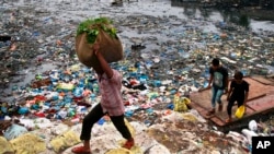 FILE - A man carries a sack of vegetables as he walks past a polluted canal littered with plastic bags and other garbage in Mumbai, India.