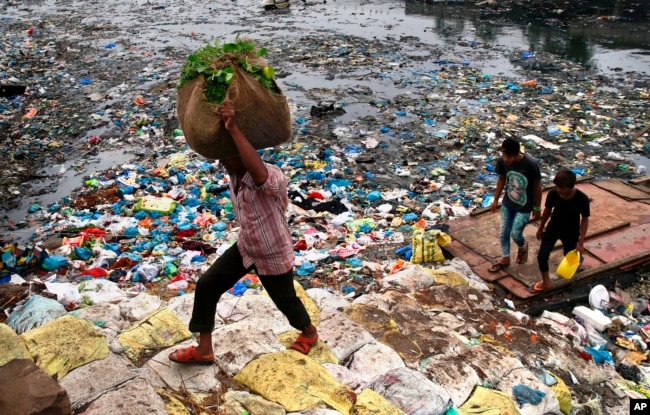 FILE - A man carries a sack of vegetables as he walks past a polluted canal littered with plastic bags and other garbage in Mumbai, India.
