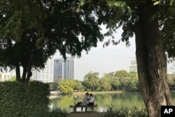In this Feb. 2, 2017, photo, a couple sit on a bench in front of a lake in Lumpini Park in Bangkok, Thailand.