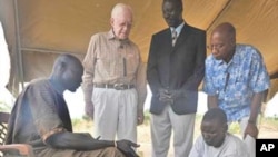 FILE - Former U.S. President Jimmy Carter, second from left, watches while a farmer with Guinea worm disease receives treatment from a volunteer trained by The Carter Center in partnership with the Government of Southern Sudan’s Guinea Worm Eradication Program, Feb. 11, 2010.