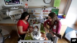 Music therapist Elizabeth Klinger, right, quietly plays guitar and sings for a baby as he grips the hand of his mother in the newborn intensive care unit at Ann & Robert H. Lurie Children's Hospital in Chicago, May 6, 2013. 