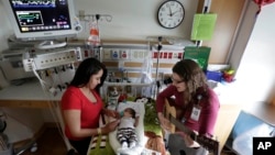 Music therapist Elizabeth Klinger, right, quietly plays guitar and sings for a baby in the newborn intensive care unit at Children's Hospital in Chicago, May 6, 2013. 