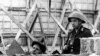 This undated 1962 file photo shows an East German People's Republic Army soldier observing a worker as he erects the Berlin Wall near Bernauer Street in Berlin, Germany.