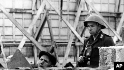 This undated 1962 file photo shows an East German People's Republic Army soldier observing a worker as he erects the Berlin Wall near Bernauer Street in Berlin, Germany.